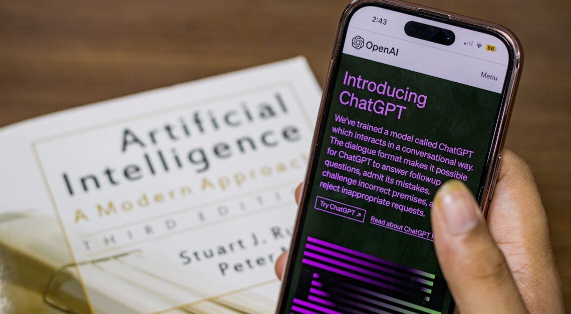 Close-up of a smartphone displaying ChatGPT app held over AI textbook.